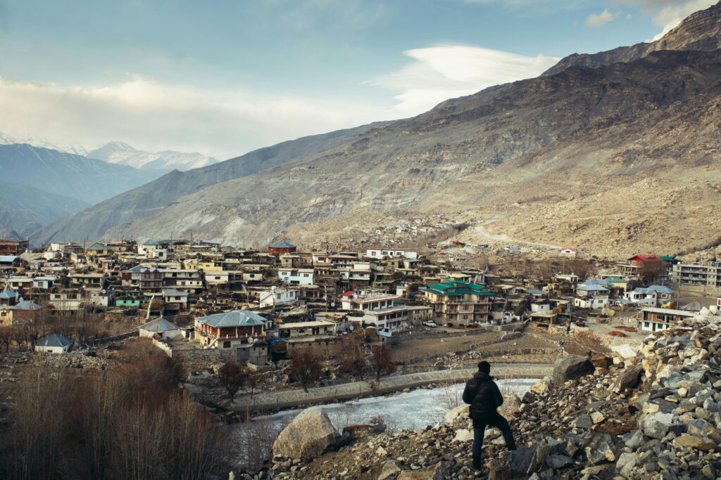 A lone traveler overlooks a picturesque mountain town in India, surrounded by rugged terrain and serene landscape.