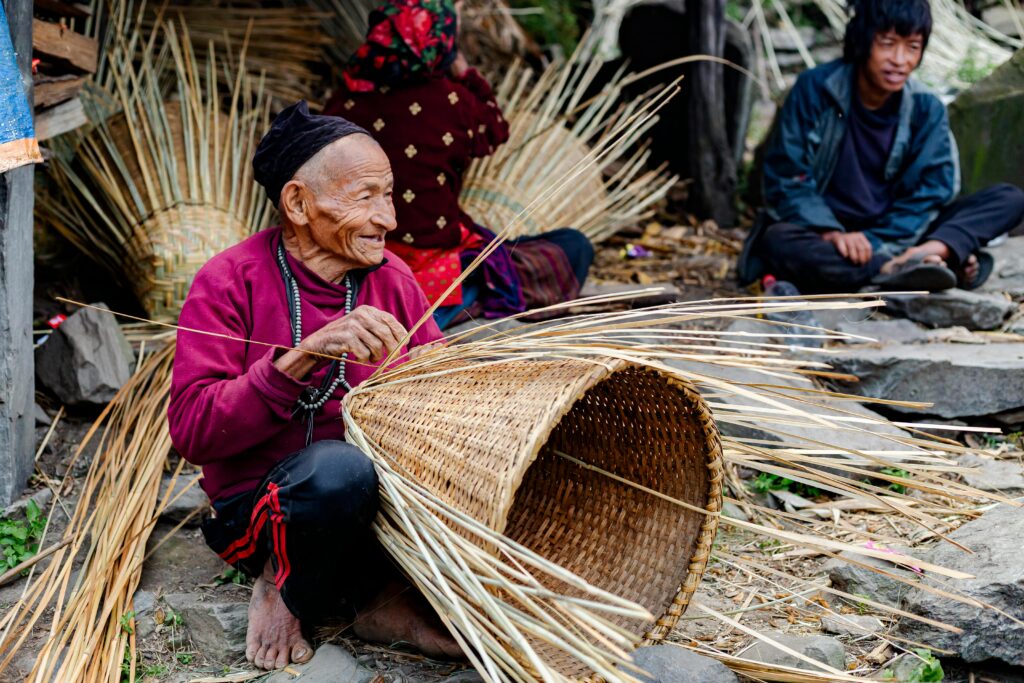 Elderly man weaving a traditional basket outdoors in Jyamrung, Nepal, showcasing village life.
