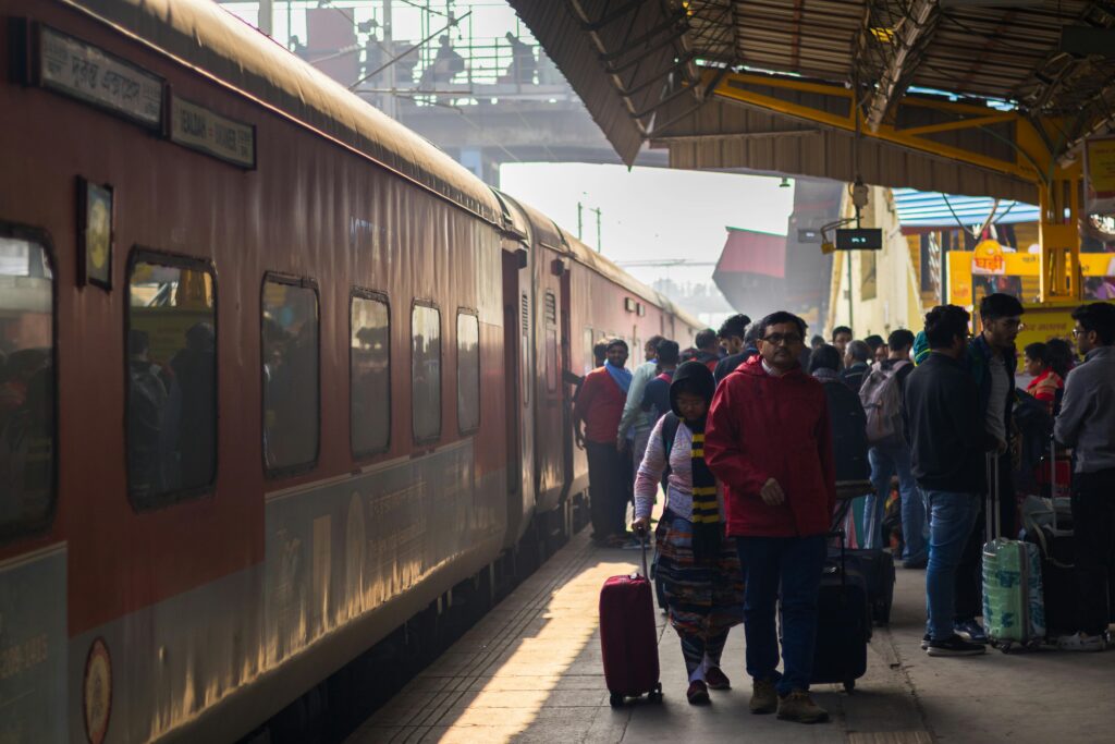 Passengers at a bustling train station platform with luggage and a stopped train.