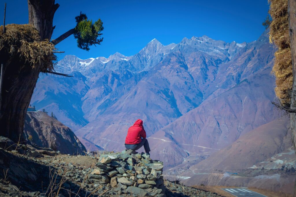 A lone traveler in a red jacket admires the vast mountain range in Juphal, Nepal.