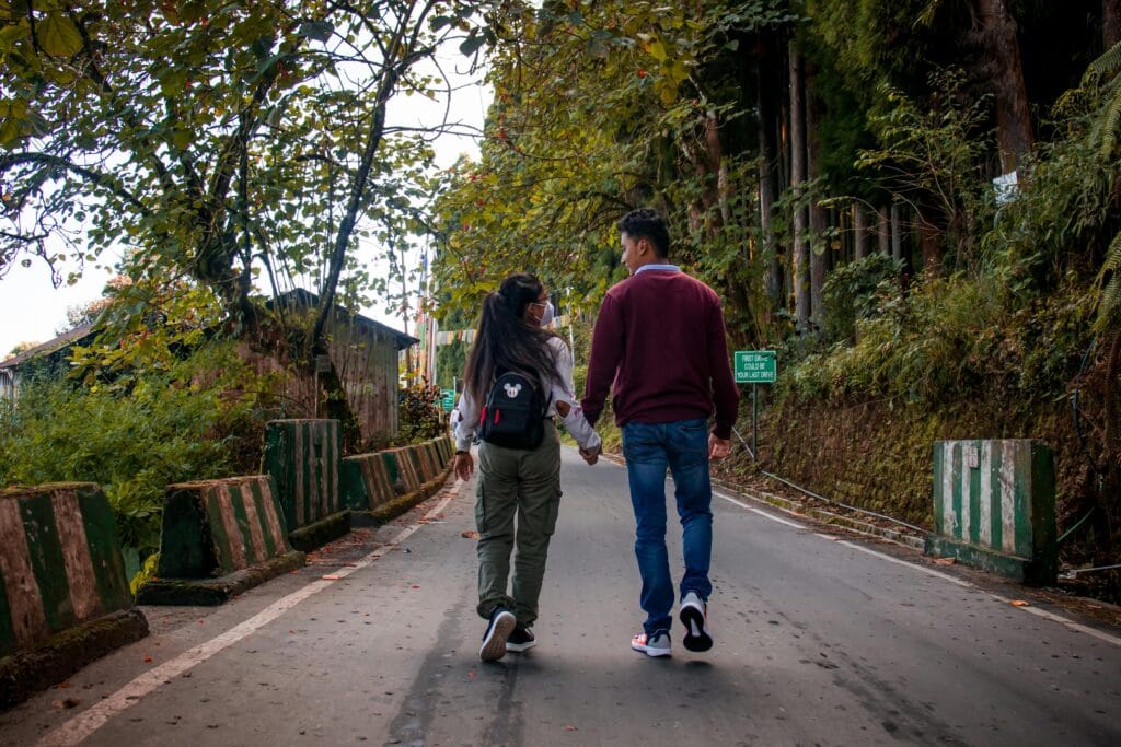A couple holding hands, walking down a scenic forest road in autumn.