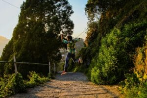 A young man jumps energetically on a scenic forest path during a sunny day.