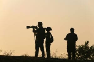 Three photographers silhouetted against a sunset sky, capturing the moment with cameras.